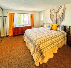 Cozy retreat with a large bed, nightstand, and dresser, plus a window with curtains and a decorative wall hanging.
