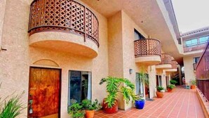 Un couloir d’hôtel avec un sol carrelé, des plantes en pot et des balcons dotés de garde-corps ouvragés.