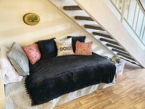 A cozy bedroom with a black bedspread, a decorative pillow with text, and a wall-mounted picture.