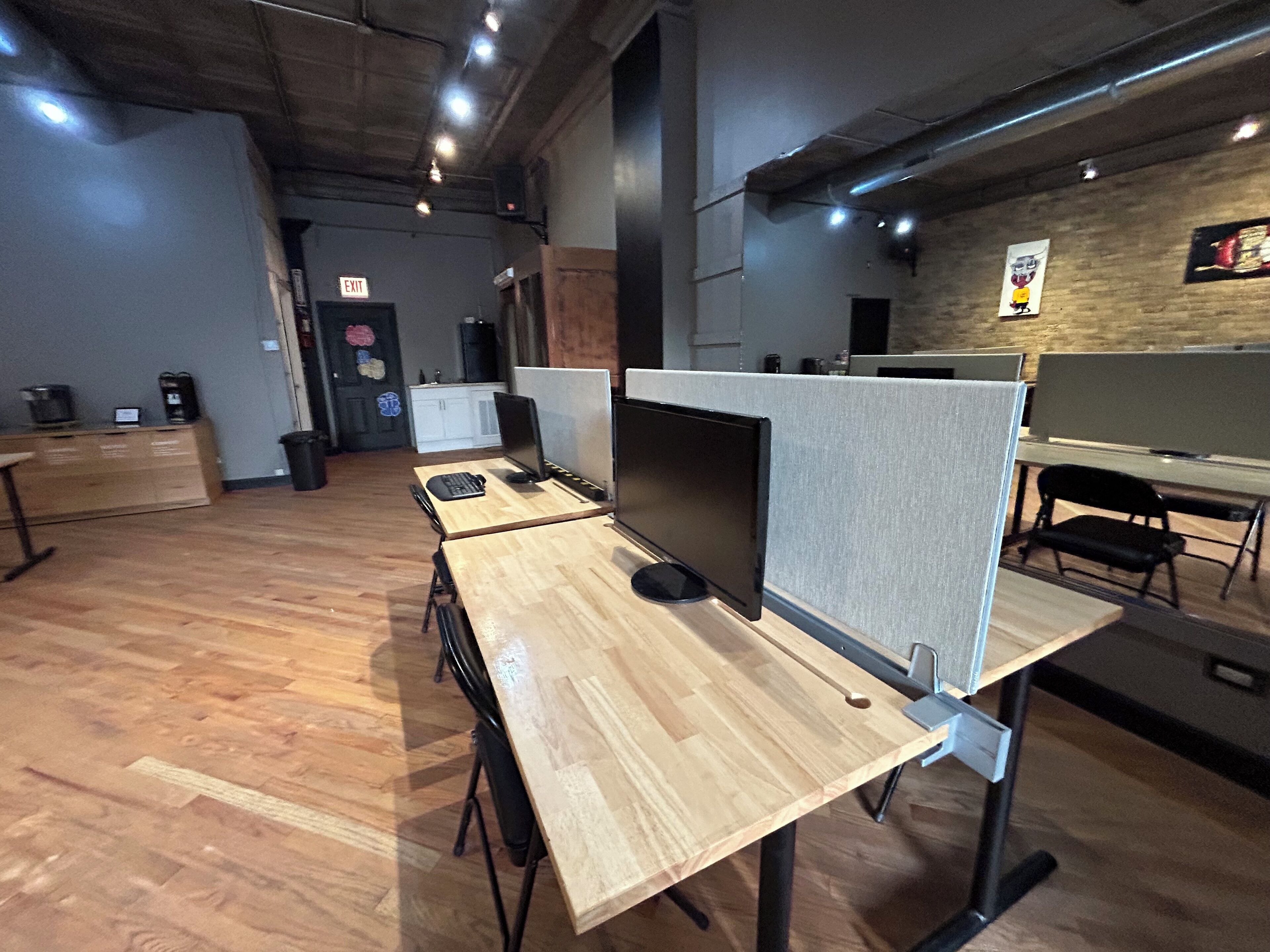 A modern office space with cubicles, wooden desks, and a brick wall.