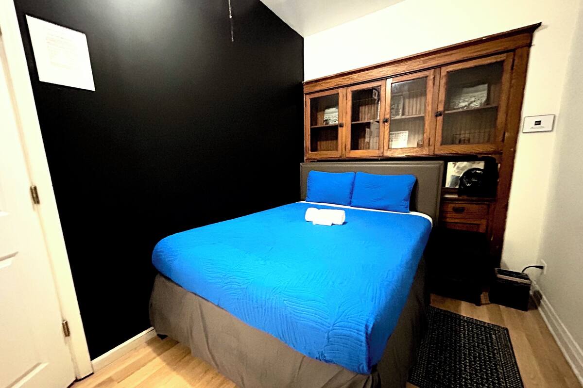 Ein kleines, gemütliches Schlafzimmer mit einem Einzelbett, einem Holzschrank und einer schwarzen Tür.