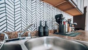 A kitchen with a stainless steel sink, two black bottles labeled "DISHER HANDS," and a herringbone-patterned backsplash. - STAY (Chicago)