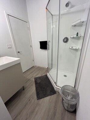 A modern bathroom with a glass shower enclosure, a white sink, and a black towel hanging on the door.