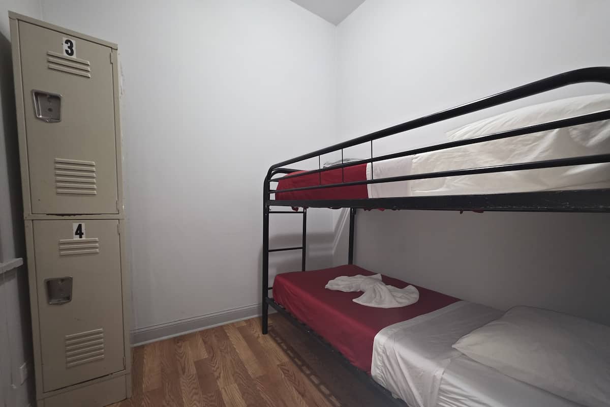 Ein Stockbett mit roter Matratze, ein Metallschrank mit zwei Fächern und ein Holzboden.