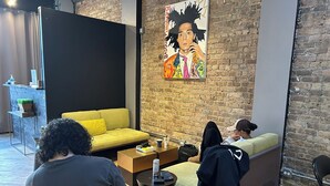 A modern lounge area with a brick wall, a yellow sofa, a black partition, and a poster on the wall. - STAY (Chicago)
