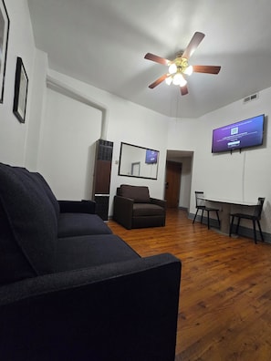 A living room with a ceiling fan, a television mounted on the wall, a sofa, a chair, and a small table. - STAY (Chicago)