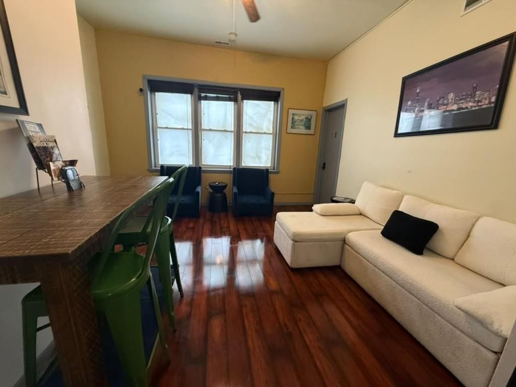 En stue med trægulv, en grøn lænestol, en beige sofa og et spisebord med stole.