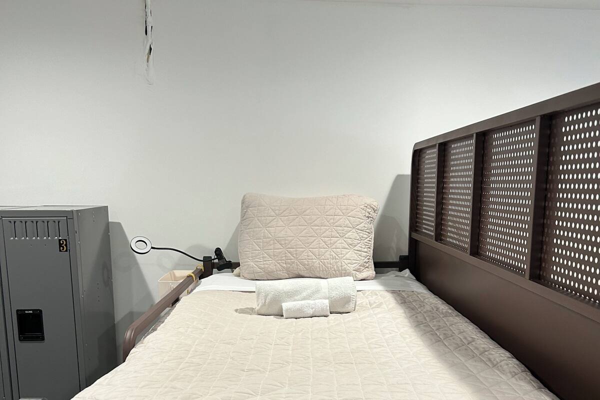 Ein Einzelbett mit einer gesteppten Matratze, einem Holzkopfbrett mit durchbrochenen Verzierungen und einem kleinen Nachttisch.