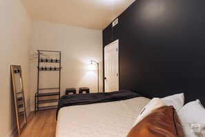 A bedroom with a bed, a bedside table, a mirror, a coat rack, and a door.