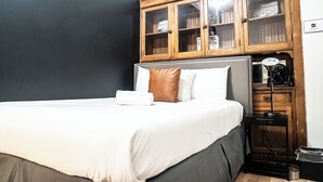 A neatly made bed with a white and brown pillow, a wooden cabinet above it, and a small black table with a lamp beside the bed. - STAY (Chicago)