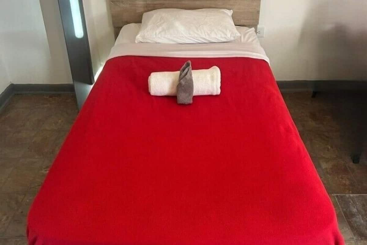 Ein Bett mit einer roten Decke und einem aufgerollten Handtuch.