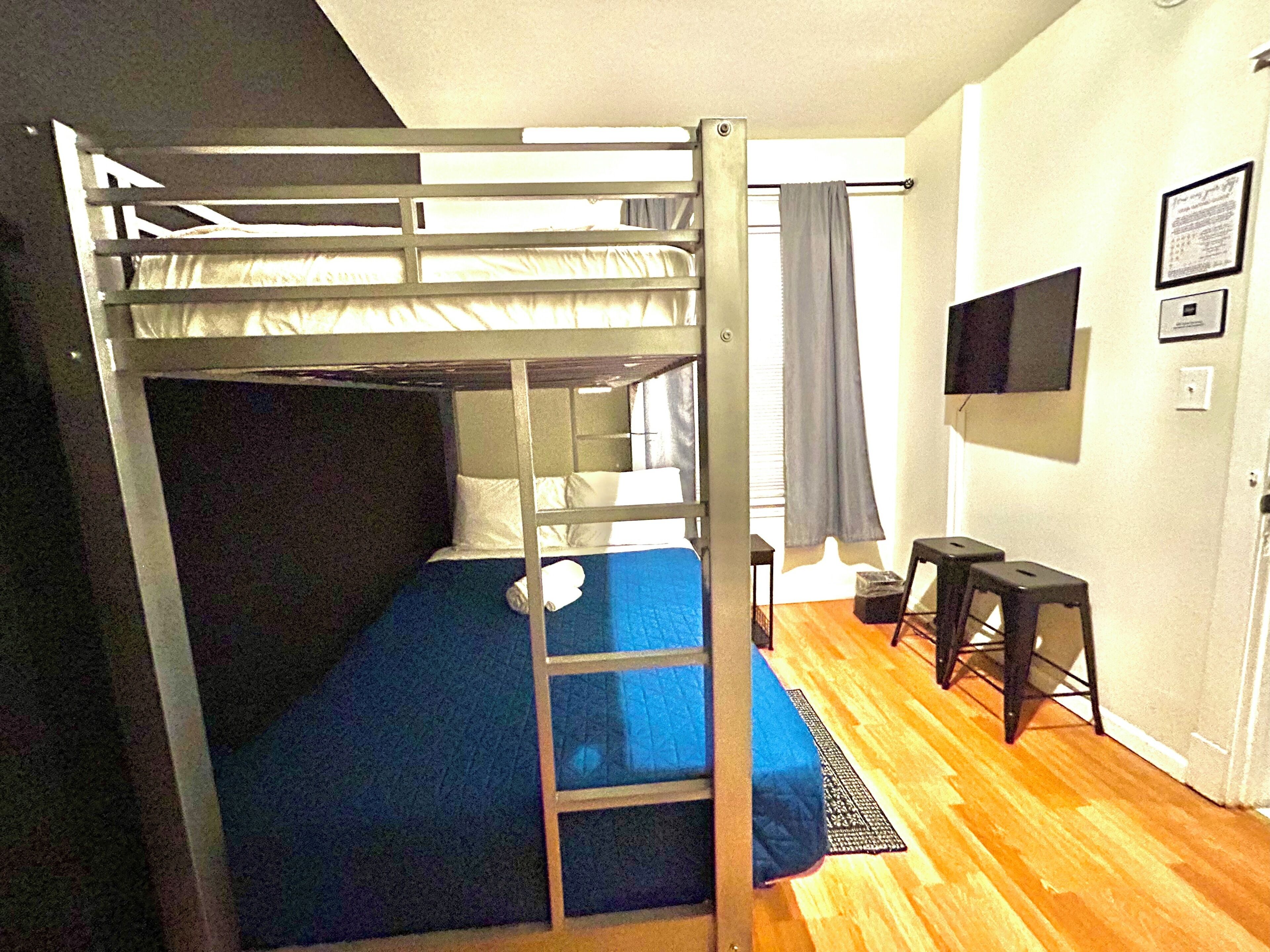 A bunk bed room with a TV, a desk, and a window with curtains.