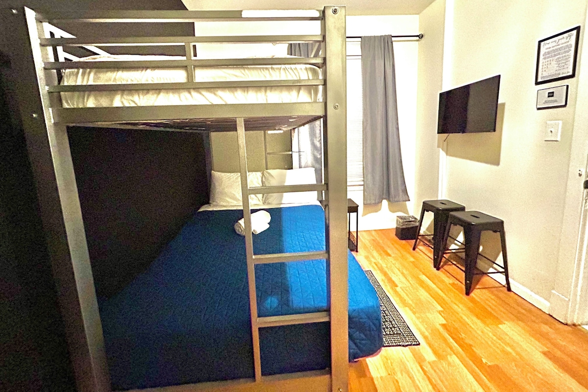 A bunk bed room with a TV, a desk, and a window with curtains.