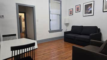 A living room with a dining table, two sofas, and a window with blinds.