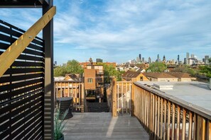 A rooftop terrace with a wooden deck, a view of the city skyline, and a staircase leading to an upper level.