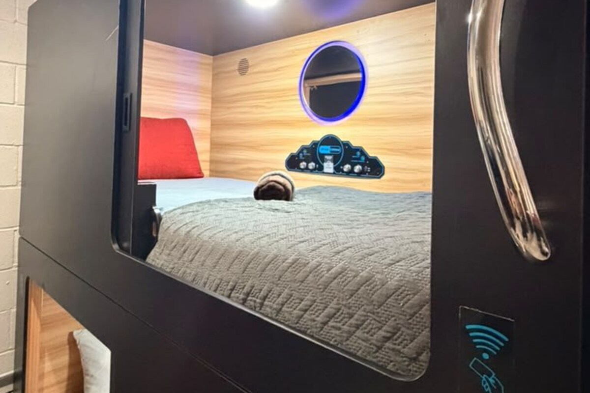 A modern room with a bed, a red pillow, a wooden headboard, and a circular mirror.