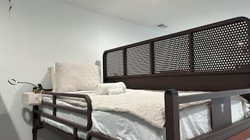 Habitación individual con una cama de madera, una mesita de noche con lámpara y un enchufe en la pared.
