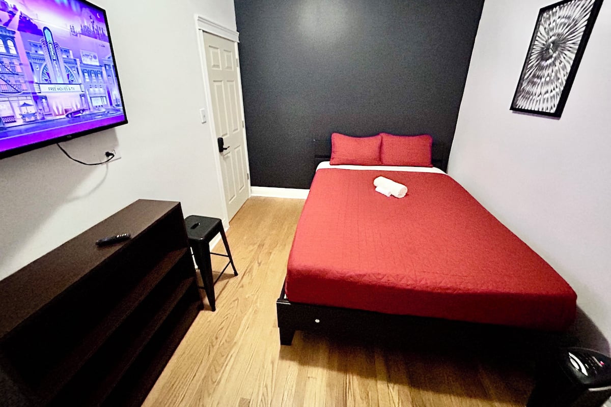 Ein Schlafzimmer mit einem Bett, einem Fernseher, einer Tür und einem gerahmten Bild an der Wand.