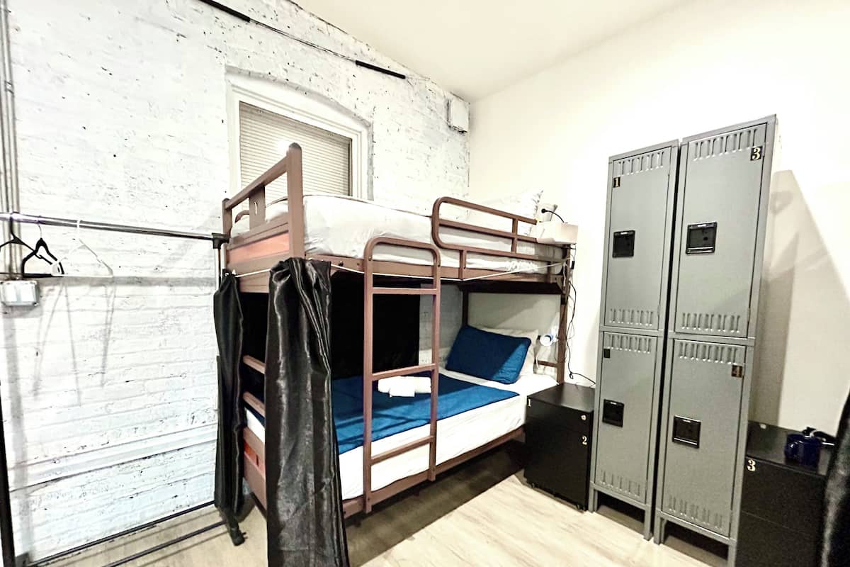 Ein Etagenbett mit blauem Kopfkissen, einem schwarzen Koffer und grauen Schließfächern.