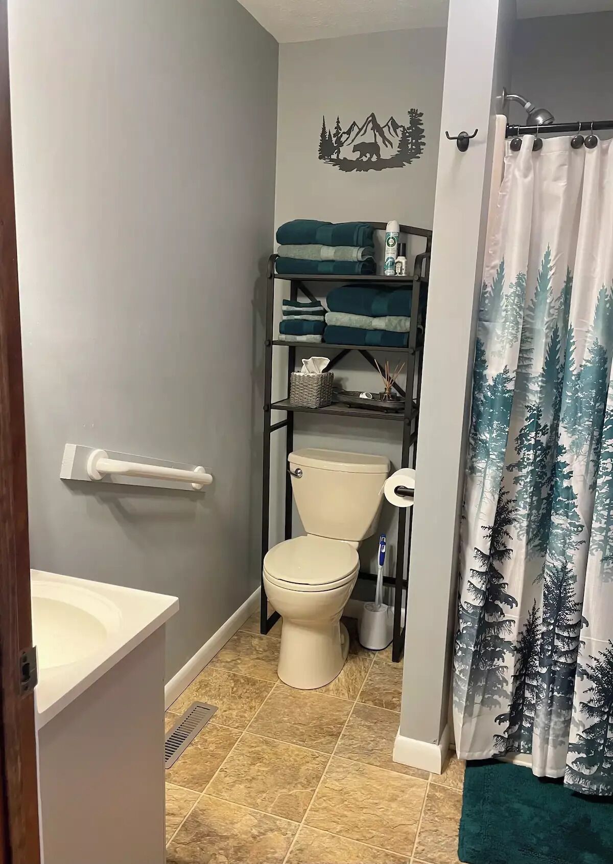 Un baño con inodoro, repisas con toallas, cortina de ducha y un adorno de pared.