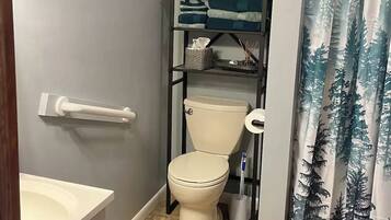 Un baño con inodoro, repisas con toallas, cortina de ducha y un adorno de pared.