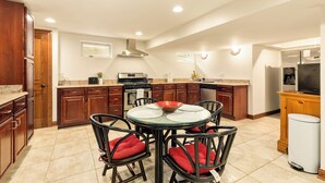 A modern kitchen with wooden cabinets, a gas stove, a dishwasher, and a dining area with a glass table and chairs. - Luxury Suite in Glen Ellyn, IL USA (Glen Ellyn)