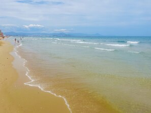 A beach with clear water, a sandy shore, and distant mountains.