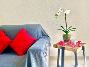 A room with a blue sofa, red pillows, a wooden side table, a potted plant, and decorative red spheres.