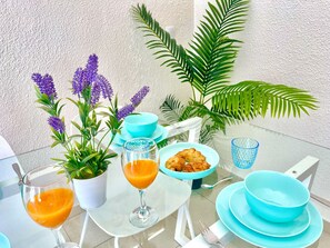 A table set with blue dishes, a glass of orange juice, a glass of orange juice, a plate of croissants, and a potted plant with purple flowers.