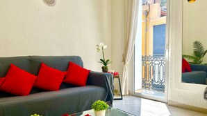 A living room with a sofa, red cushions, a glass coffee table with plants, and a view of a balcony with a railing. - San Francisco Home by Gloove (Alicante / Alacant)