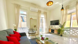 A living room with a sofa, a glass coffee table, a chair, a TV, and a balcony with curtains. - San Francisco Home by Gloove (Alicante / Alacant)