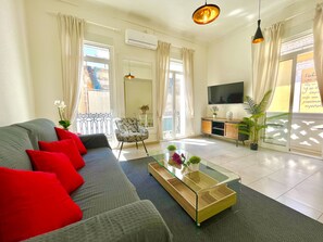 A living room with a sofa, a glass coffee table, a chair, a TV, and a balcony with curtains.