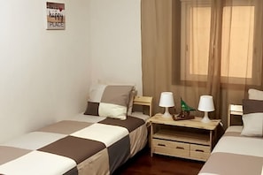 A hotel room with two single beds, a small wooden nightstand with a lamp, a decorative item, and a sheer curtain covering a window. - Casa Alba Mindelo (Vila do Conde)