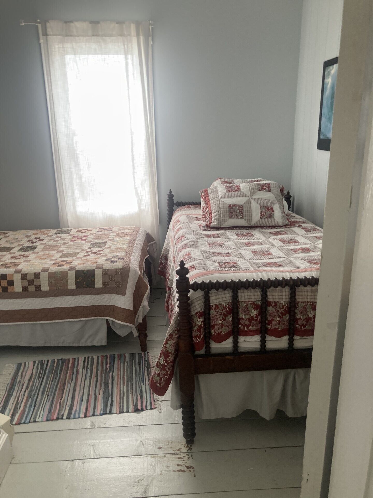 A bedroom with two beds, a window with sheer curtains, and a striped rug.