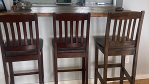 A kitchen with a breakfast bar, three wooden chairs, and a window with a view of greenery.