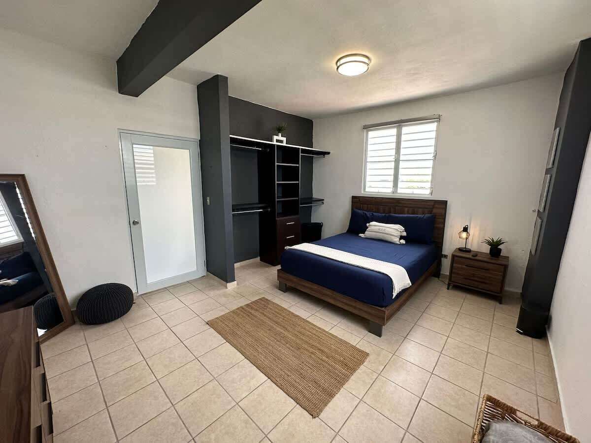 Un dormitorio con cama, armario, mesita de noche y ventana.