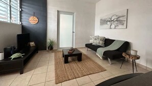 A modern living room with a sofa, coffee table, TV, and a painting on the wall. - City Charm: Double BR San Juan Adventure, Sleeps 2 (San Juan)