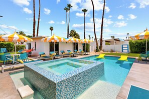 Una piscina con borde de azulejos, sillas de descanso y sombrillas.