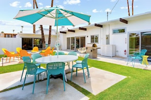 Un espace patio aménagé avec une table ronde et des chaises, un grand parasol et un barbecue.
