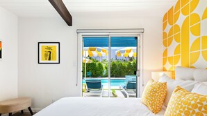 Ein Hotelzimmer mit einem großen Bett, Blick auf einen Swimmingpool und einem Balkon mit Sitzgelegenheit.