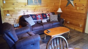 Ein gemütliches Blockhaus-Interieur mit Holzwand, Ledersofa, Couchtisch aus Holz und einer Stern-Dekoration.