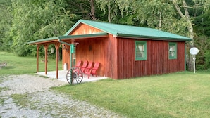 Eine Holzhütte mit einem grünen Dach und einer Veranda, auf der rote Stühle stehen.