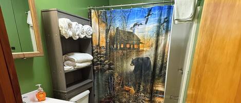 A bathroom with a green wall, a wooden vanity, a white toilet, and a shower curtain depicting a bear and birds.