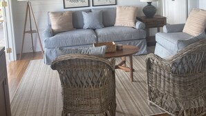 A cozy living room with a wooden ceiling, a grey sofa, wicker chairs, and framed botanical prints on the wall. - Charming Nevis Cottage with pool and ocean view on grounds of Hermitage Inn (Gingerland)