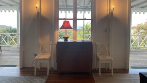 A room with a wooden ceiling, a window with a red lamp, two white chairs, and a wooden desk. - Charming Nevis Cottage with pool and ocean view on grounds of Hermitage Inn (Gingerland)