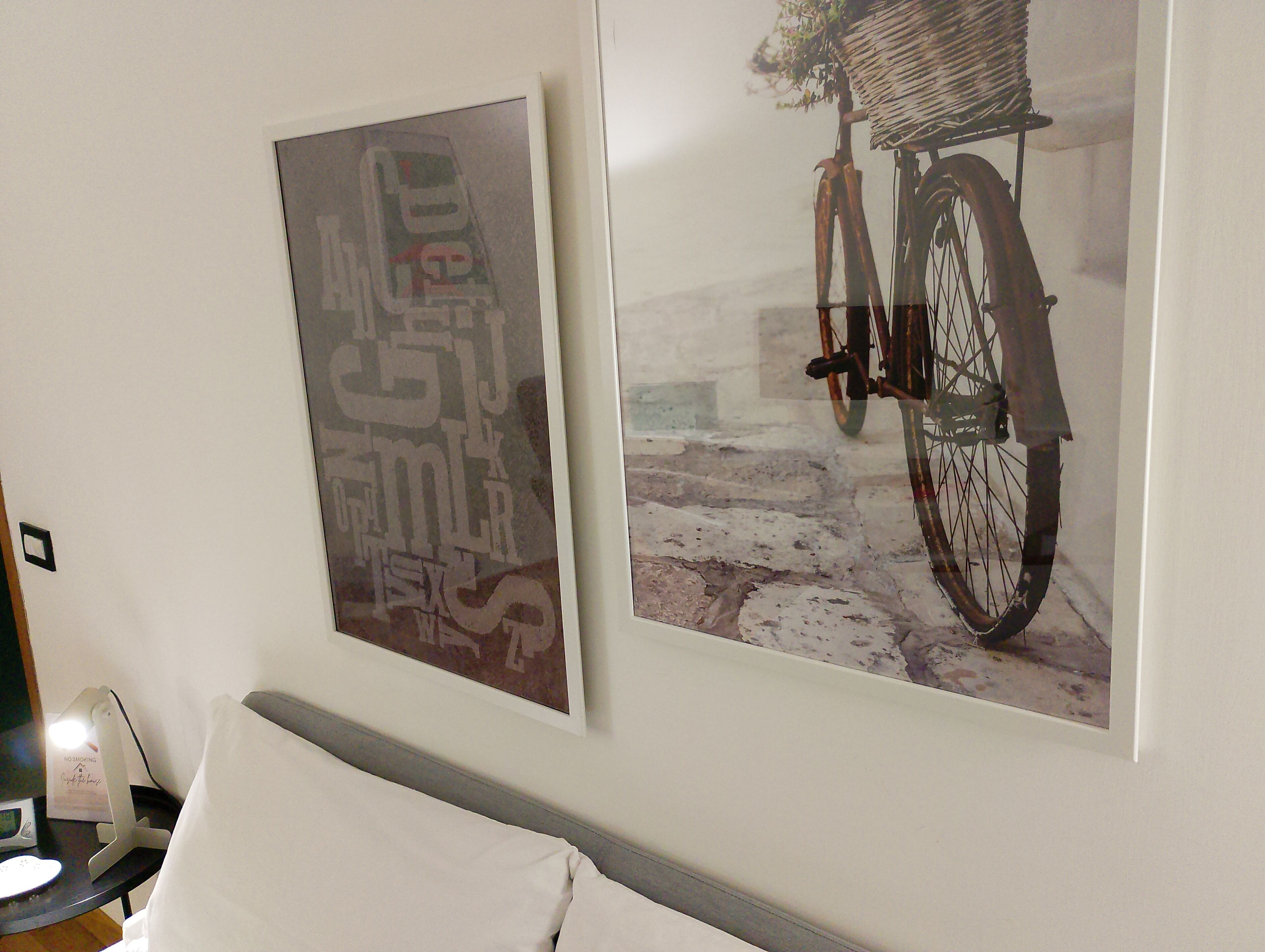 Two framed artworks on a wall, a poster with abstract text and a bicycle illustration.