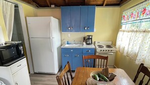 A compact kitchen with blue cabinets, a white refrigerator, a stove, and a dining table with chairs.