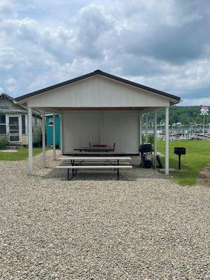 Un espace pique-nique abrité, doté de bancs et d’un barbecue, entouré de gravier et d’une pelouse.