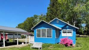 A blue house with a white bench and pink flowers in the yard.