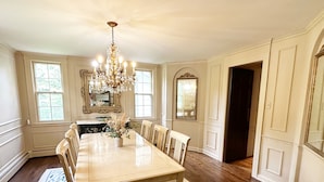 A dining room with a large table, chairs, a chandelier, and a patterned rug.